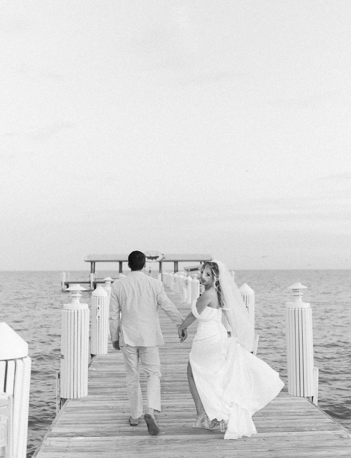 The newlyweds laugh and hold hands as they run along the wooden dock, capturing the excitement of their Florida Keys wedding.
