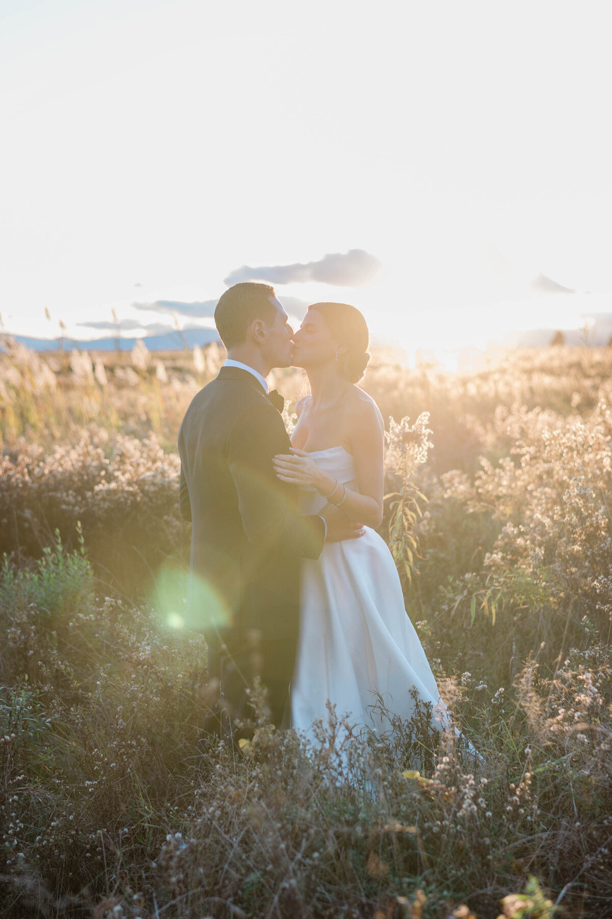 The couple shares a kiss amidst tall wildflowers, bathed in golden sunset light