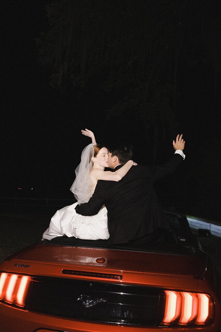 bride and groom kiss  on top of  convertible  getaway car