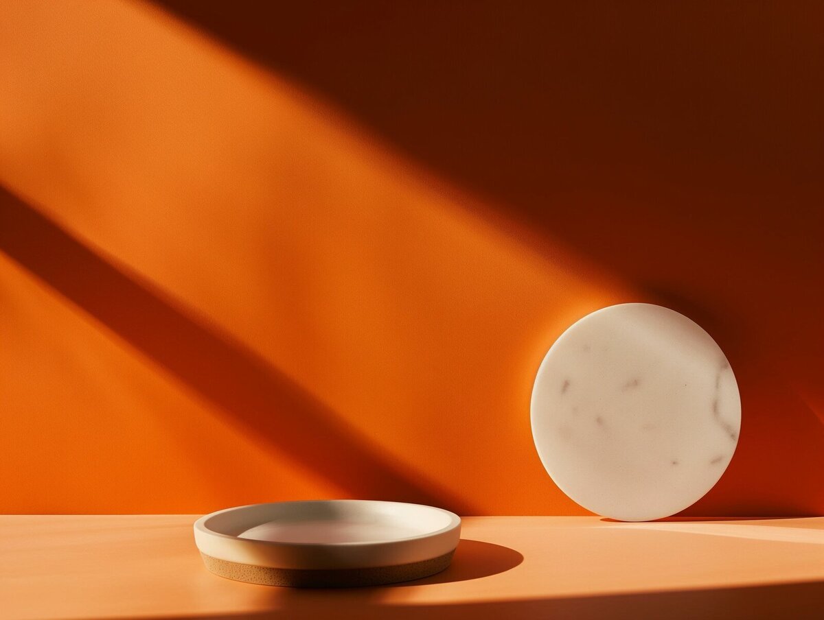 Minimal scene with two round ceramic objects against an orange wall, with dramatic shadows and warm sunlight.