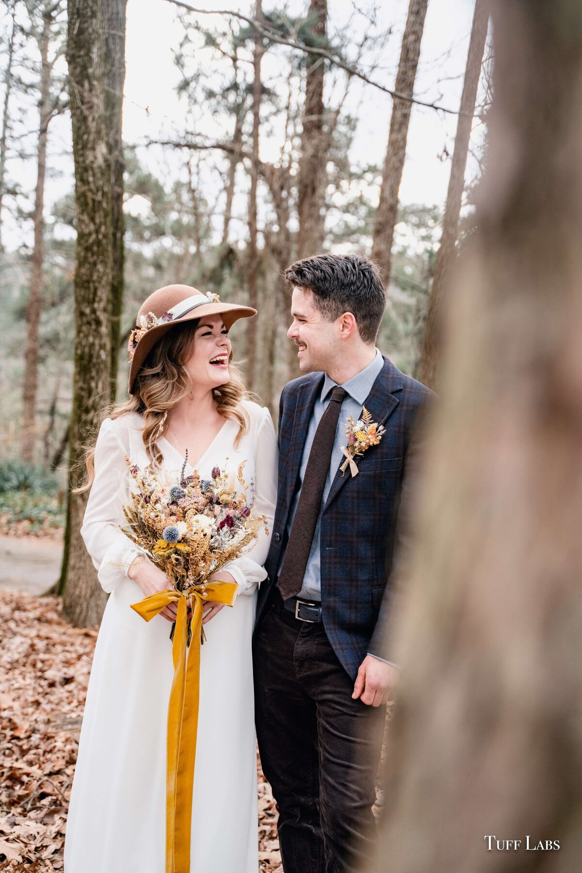 Bride and groom smile at one another and she is holding her dried flowers bouquet at their outdoor winter wedding.