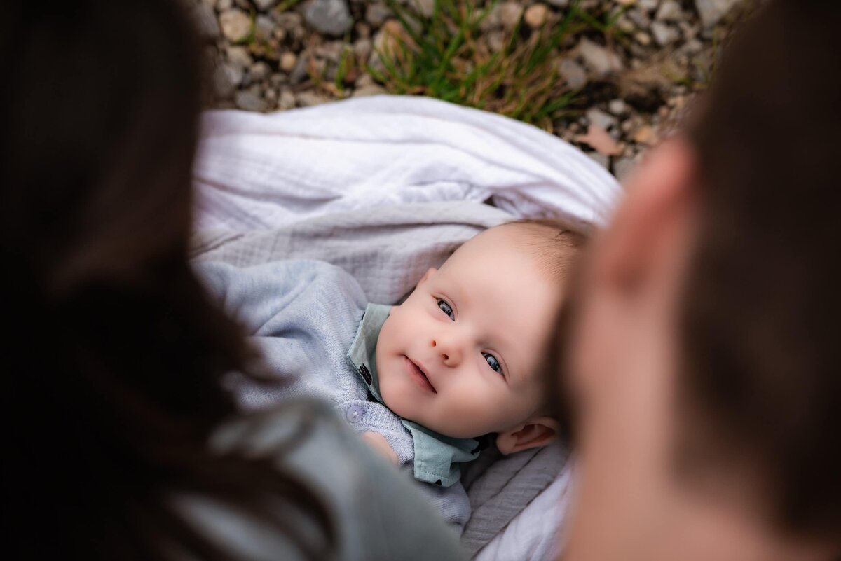 baby lying on white blanket looking up at parents