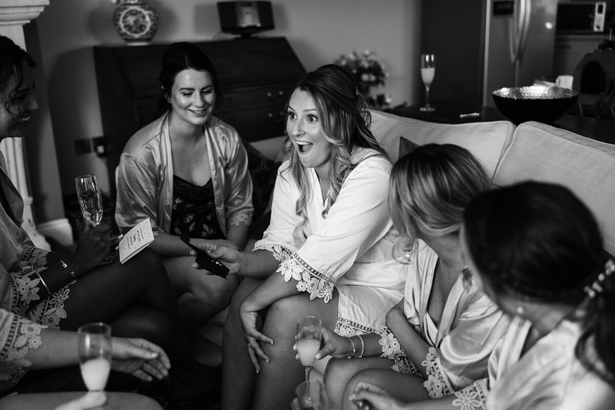 Black and white Informal photo of a bride and her bridesmaids enjoying opening gifts together