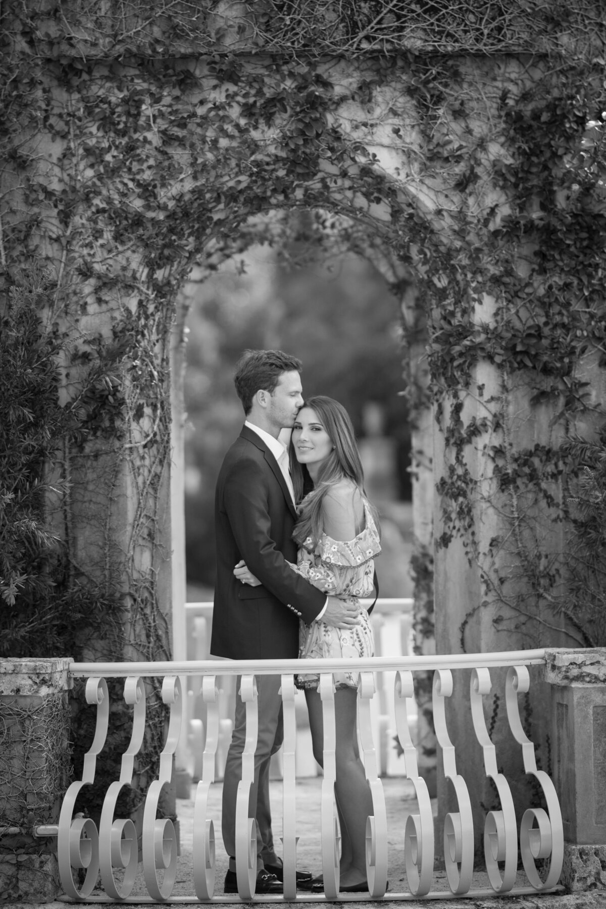 A couple shares a loving embrace beneath a romantic stone archway.