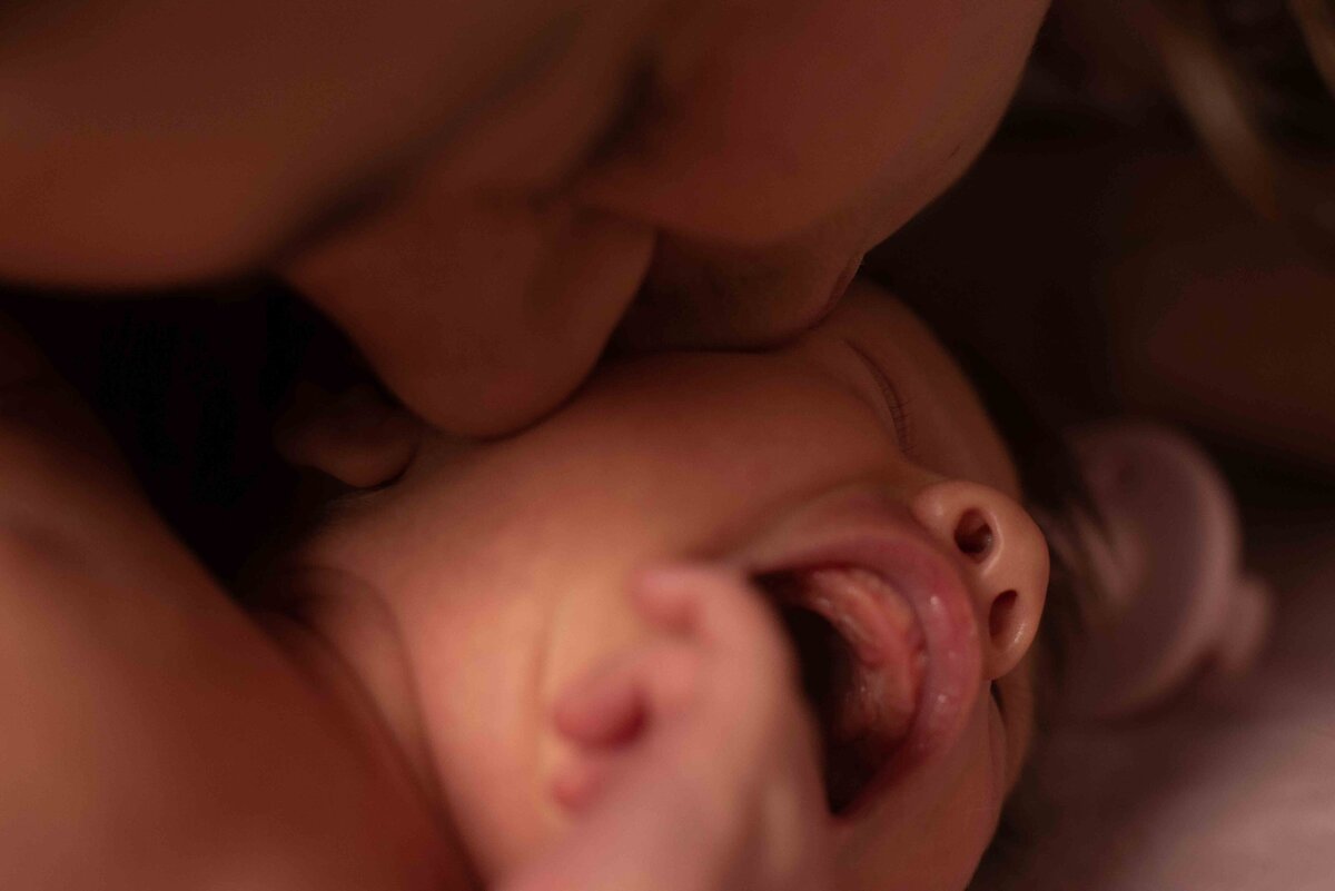 a crying newborn has its cheek kissed by the new mother
