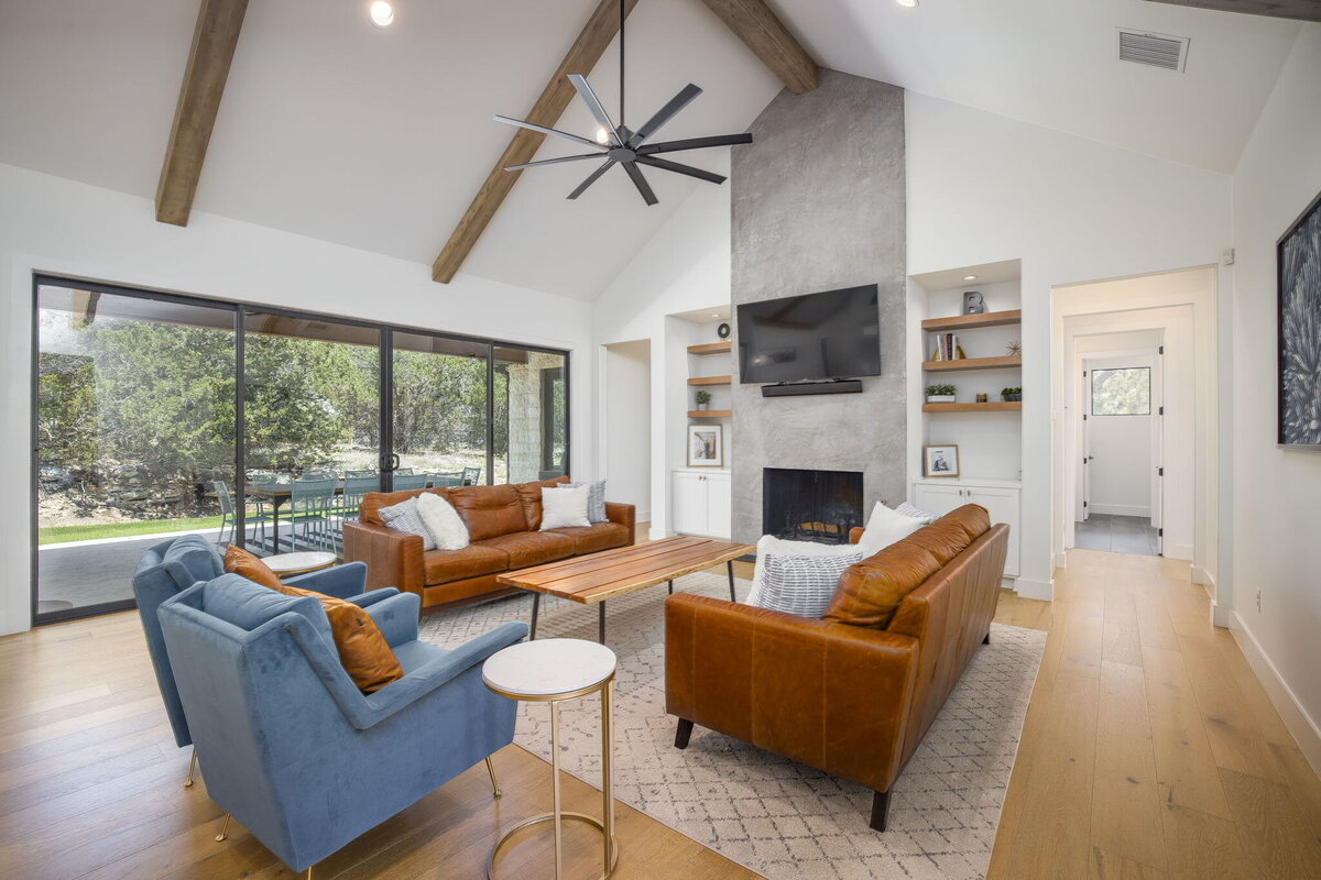 stucco fireplace in the center of modern living room with vaulted ceiling, wood beams and sliding glass doors