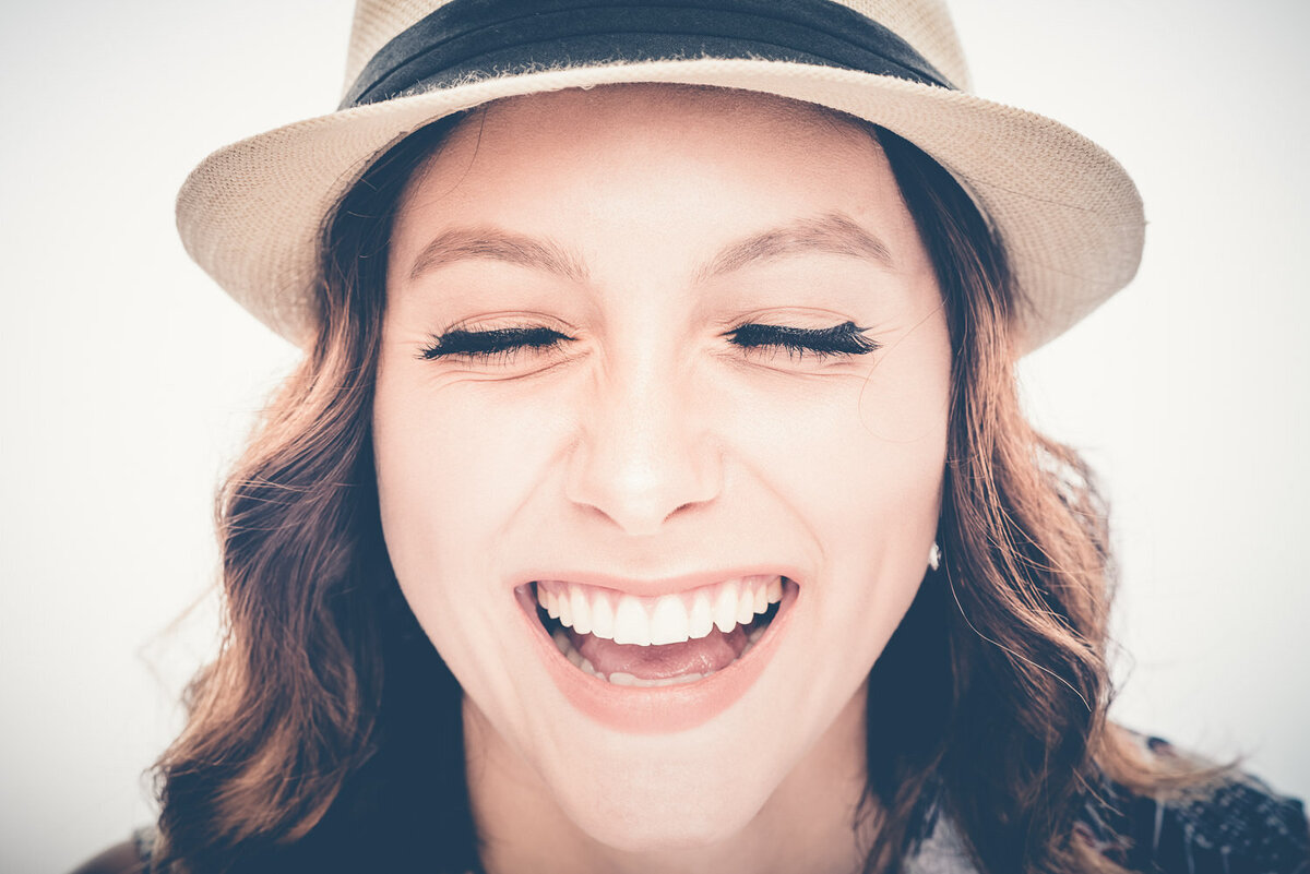 Close-up personal branding portrait of a woman smiling and wearing a stylish fedora.