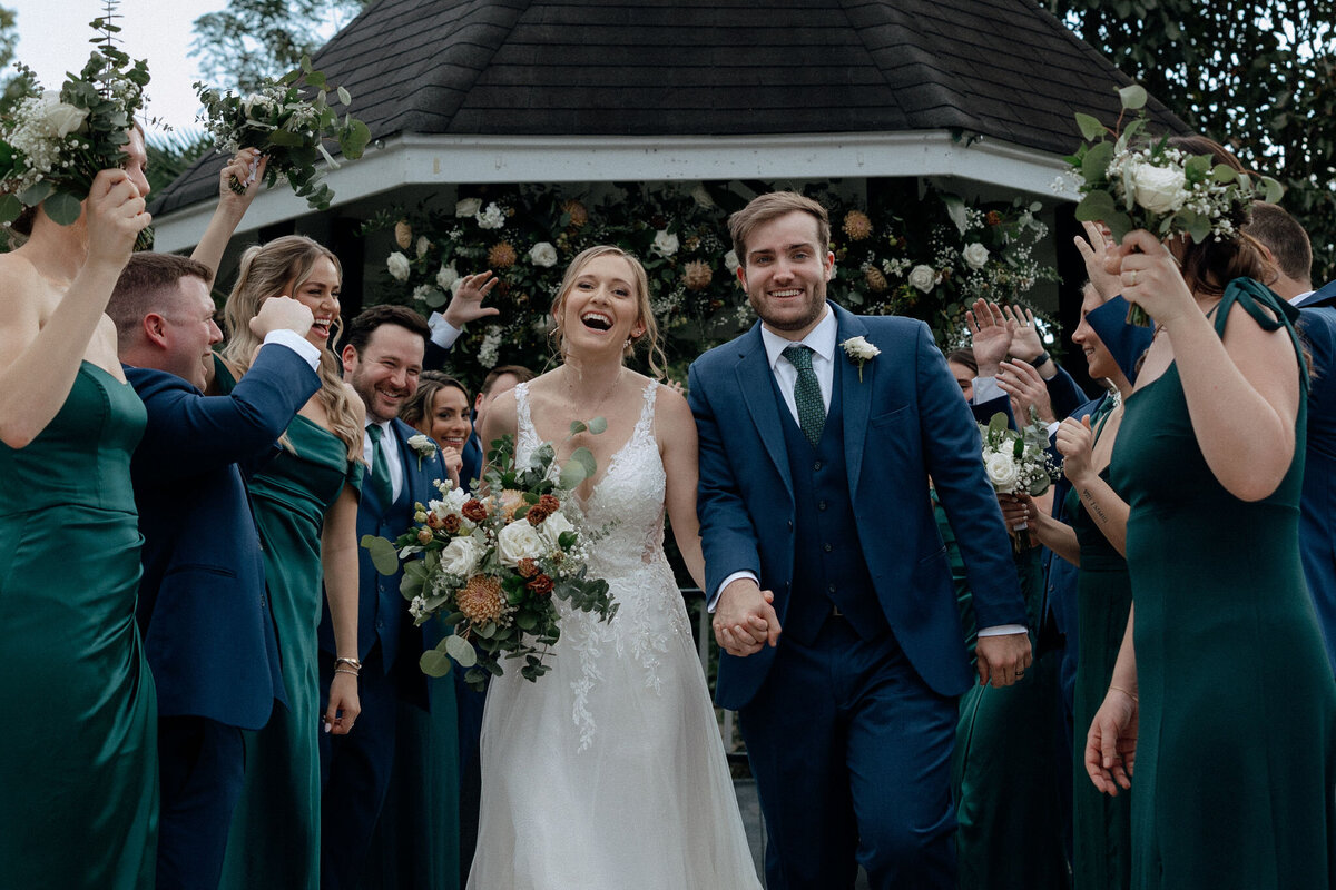 A bride and groom run through a tunnel made by their bridesmaids and groomsmen as they cheer them on.