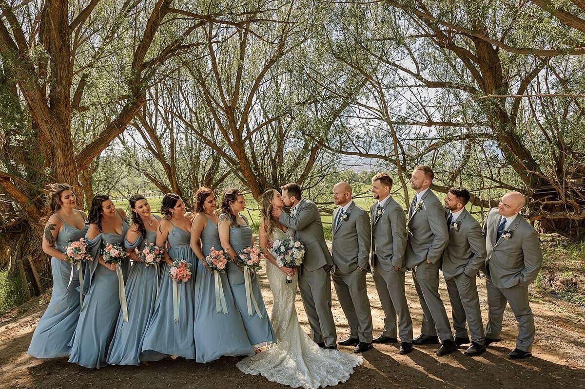 Bridal party group photograph with couple kissing and friends smiling at them