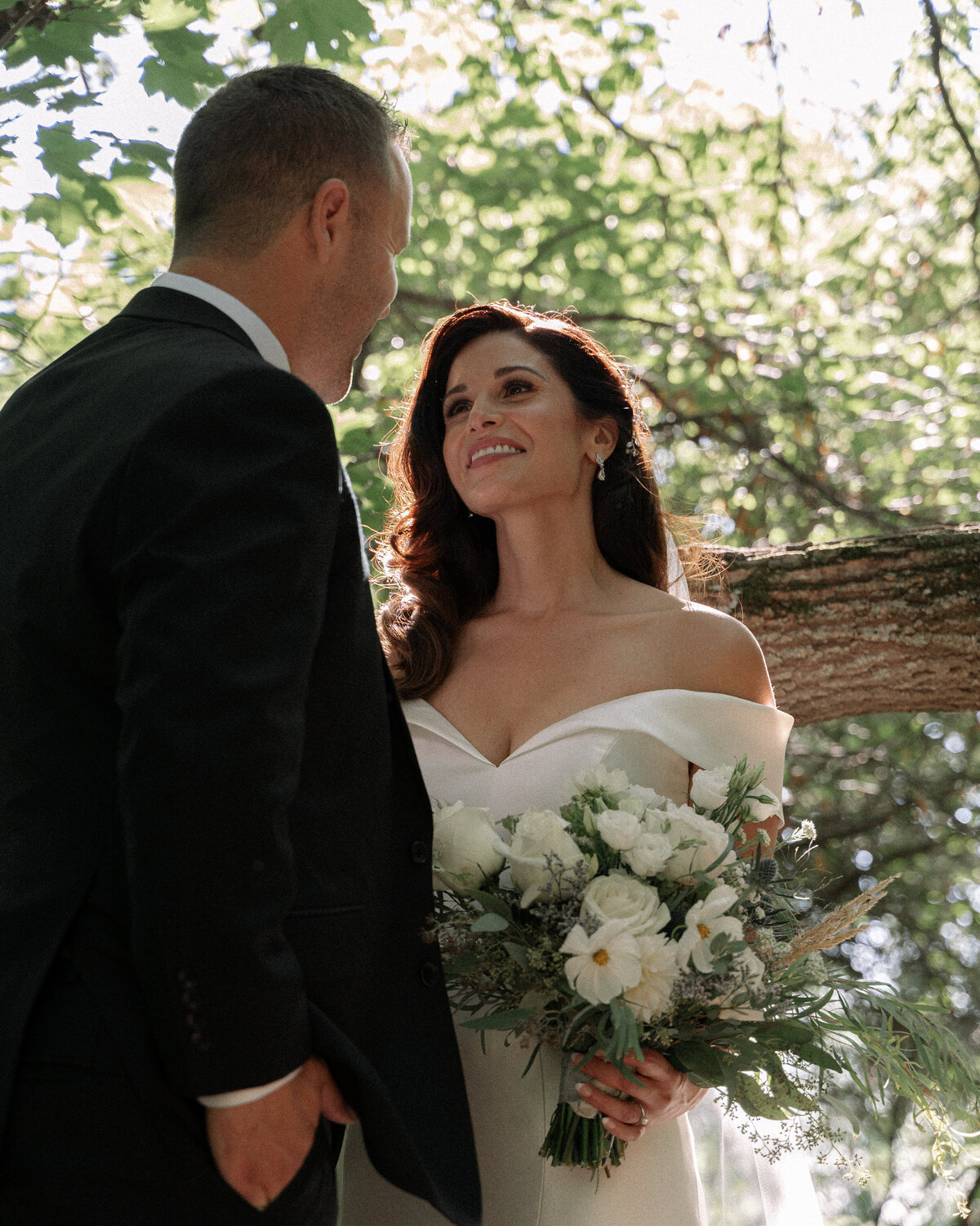 bride looks deeply into grooms eyes in a canopy of trees
