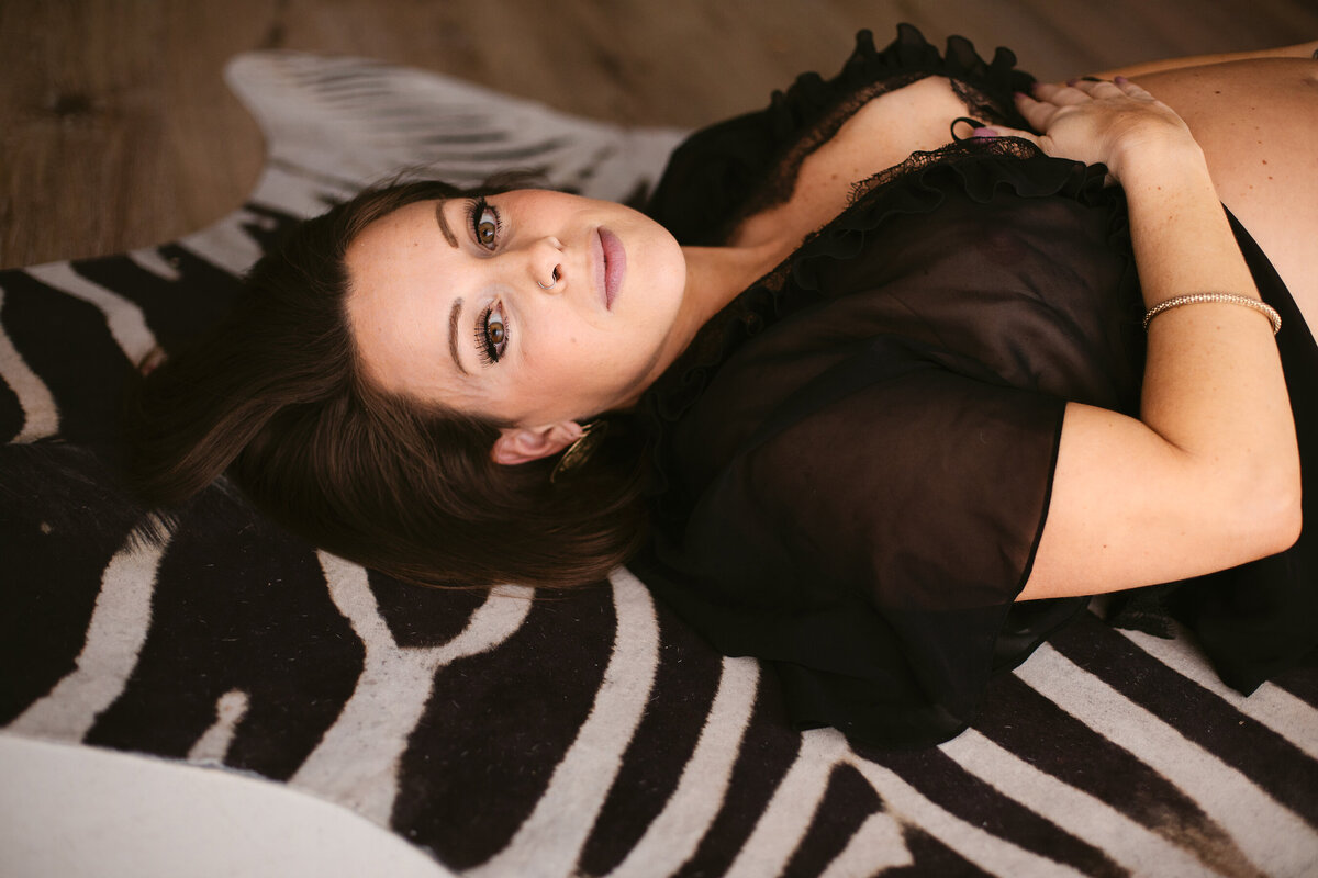 A stunning woman in black lingerie lays peacefully on a zebra rug during a Bentonville boudoir photoshoot.