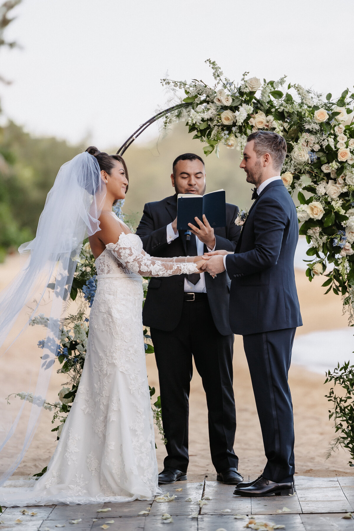 Bride and groom ceremony at Kualoa Ranch on the beach, holding hands with palm trees and ocean in the background