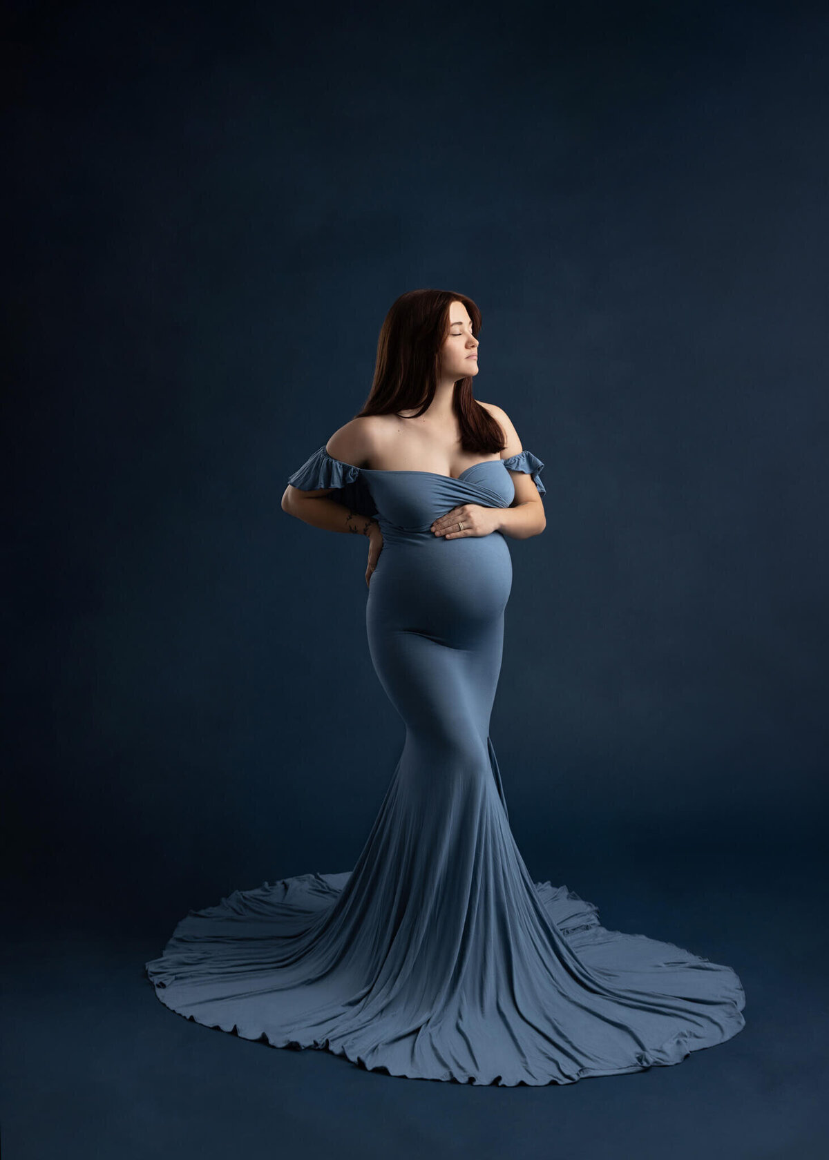pregnant woman  wearing a blue dress with her hand on the top of her belly