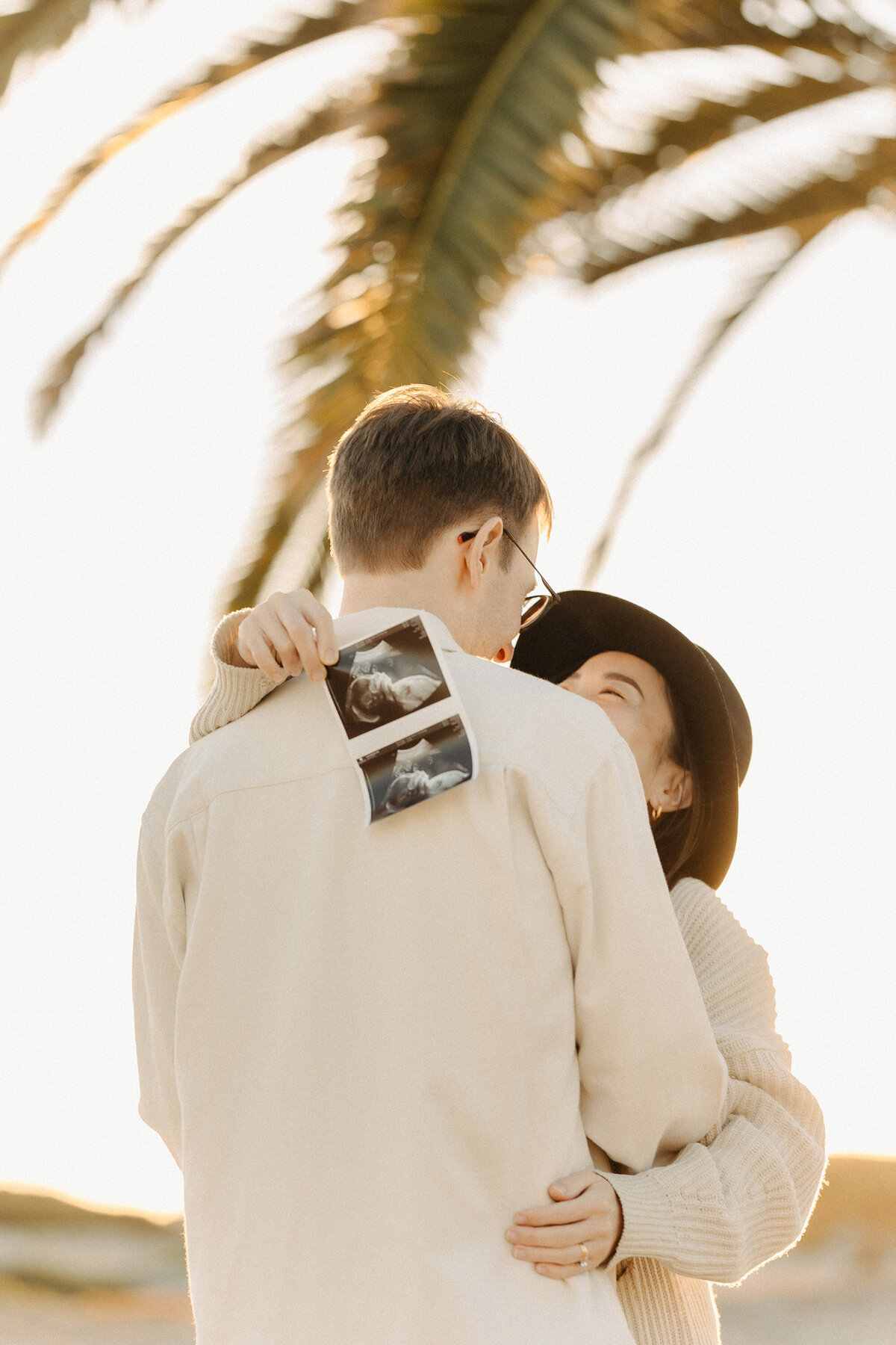 Couple hugging at Coronado Beach with baby ultrasound photo tucked in the father’s pocket during a maternity photoshoot. Captured by San Diego Family Photographer Yuka Schad.