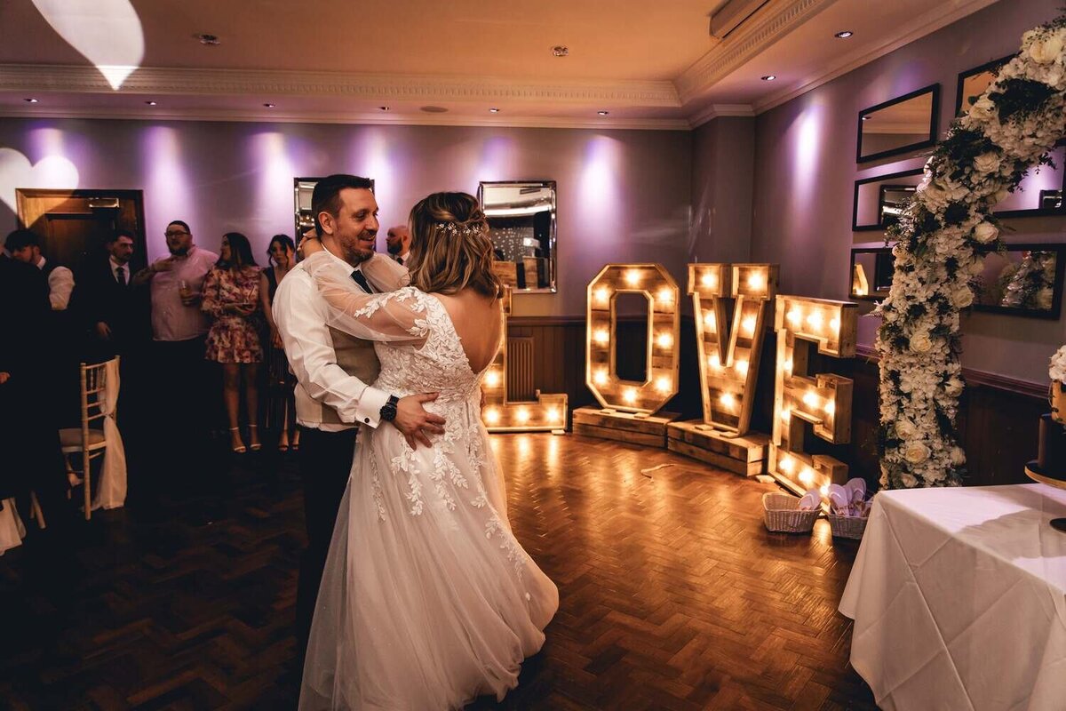 Bride and Groom first dance in front of lights in the shape of the letters LOVE