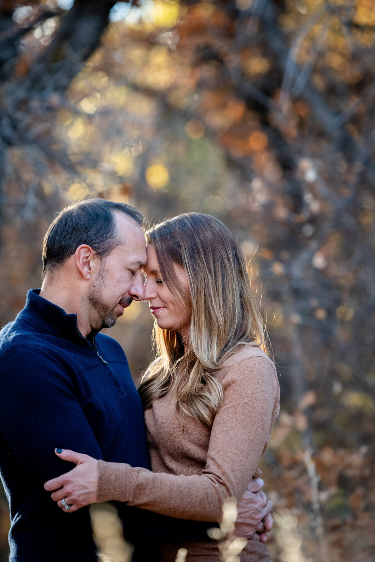 Happy couple touch foreheads while snuggling in a forest at sunset