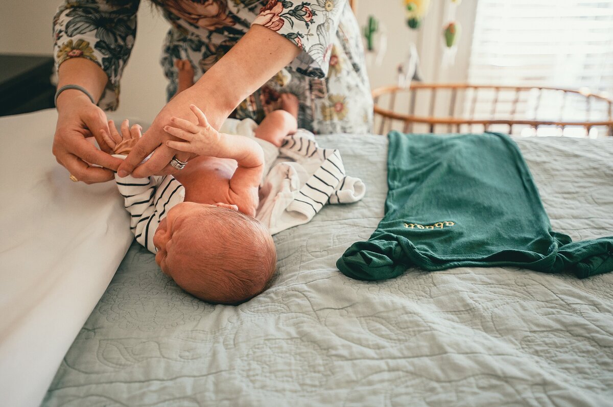 Mom changing baby on bed during their Cypress Newborn Photography session