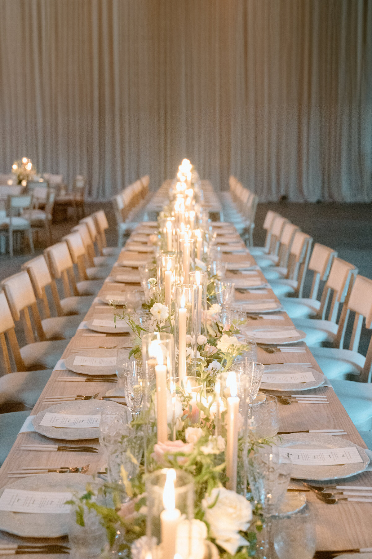 Long banquet-style wedding table with rows of candles and elegant florals.