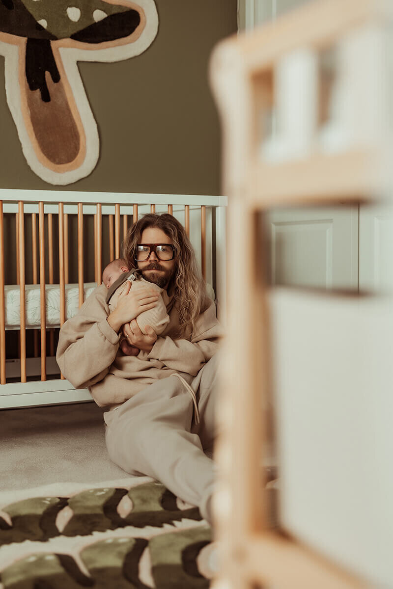 Dad sitting against baby's crib while holding his new son over his shoulder