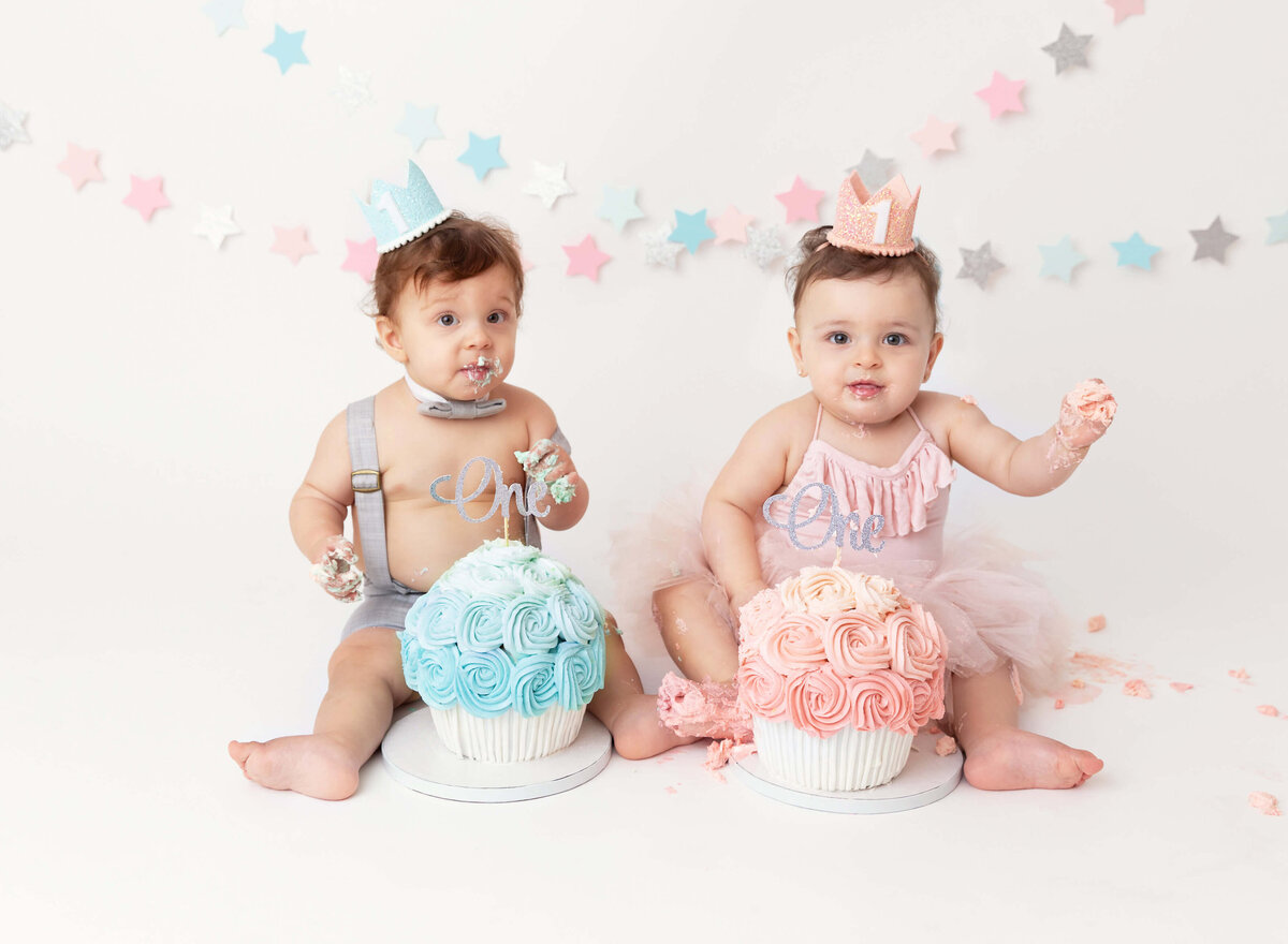 Twins cake smash session boy and a girl, celebrating their first birthday with custom blue and pink cakes. Perfect for documenting this special milestone in NYC