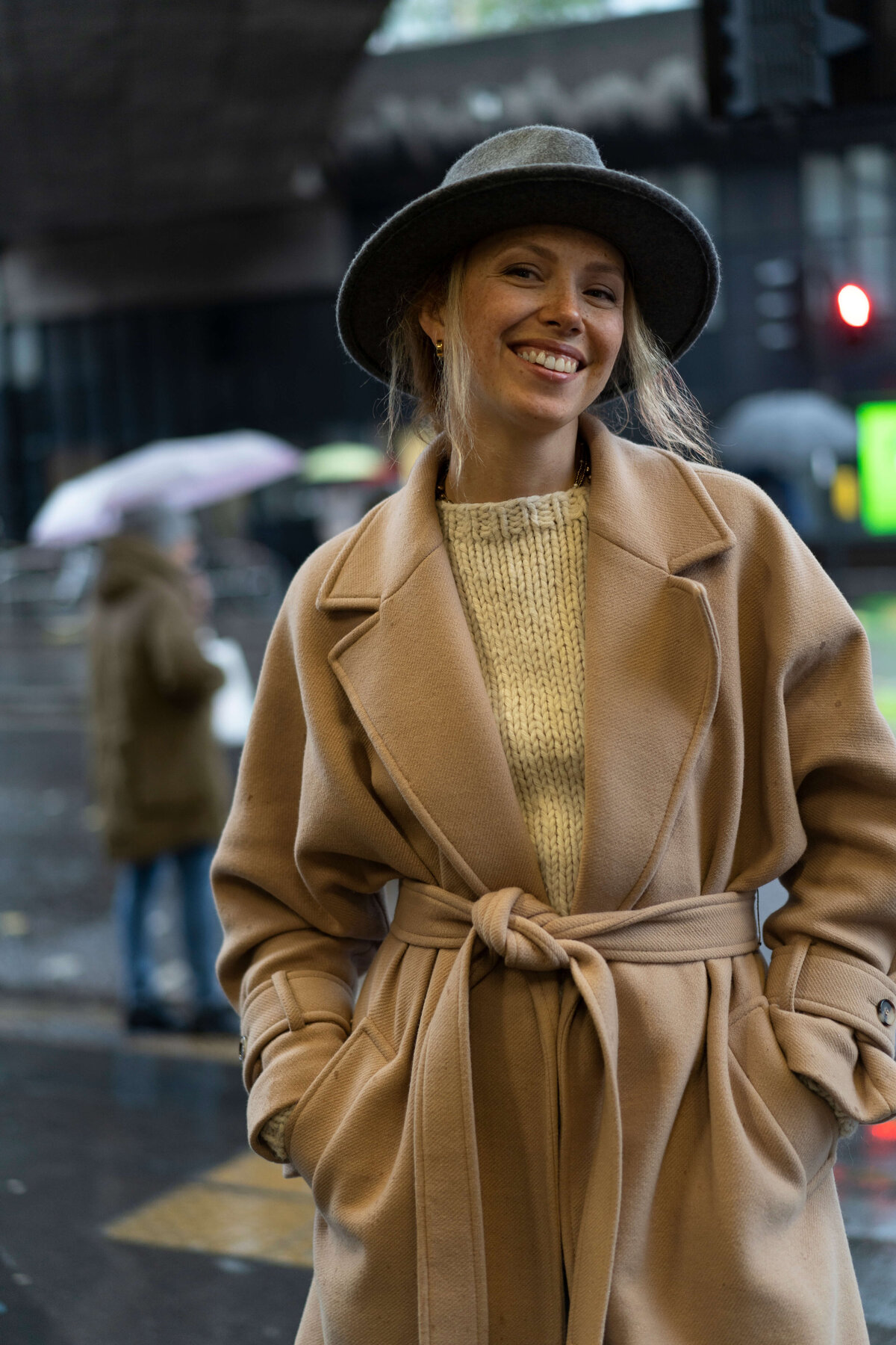 A woman in a long beige coat and a hat in the rain in London