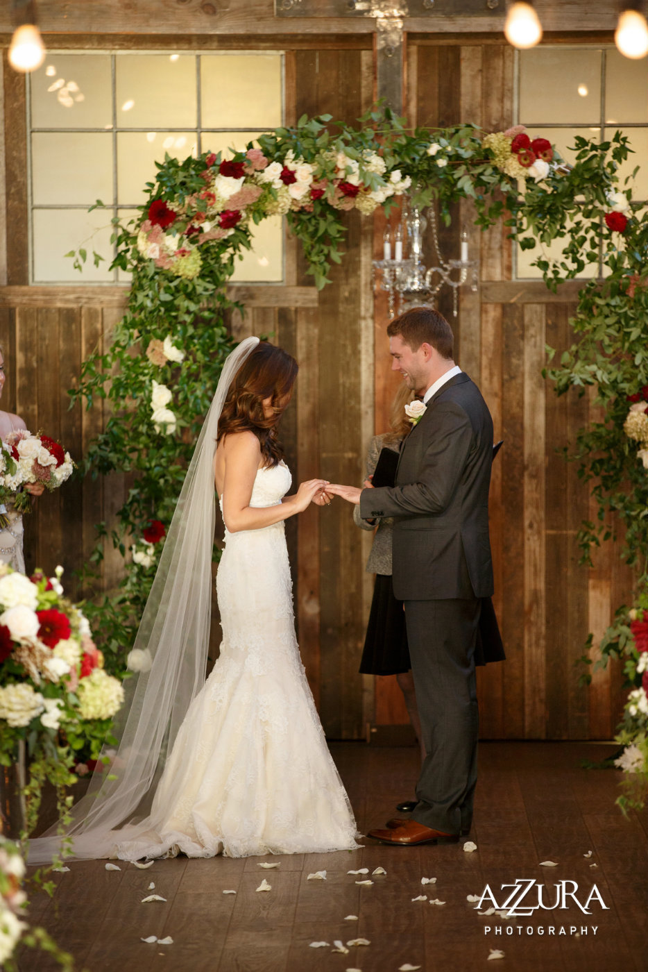 bride and groom in front of wedding arch covered in greenery and red and white flowers at fall wedding Sodo Park
