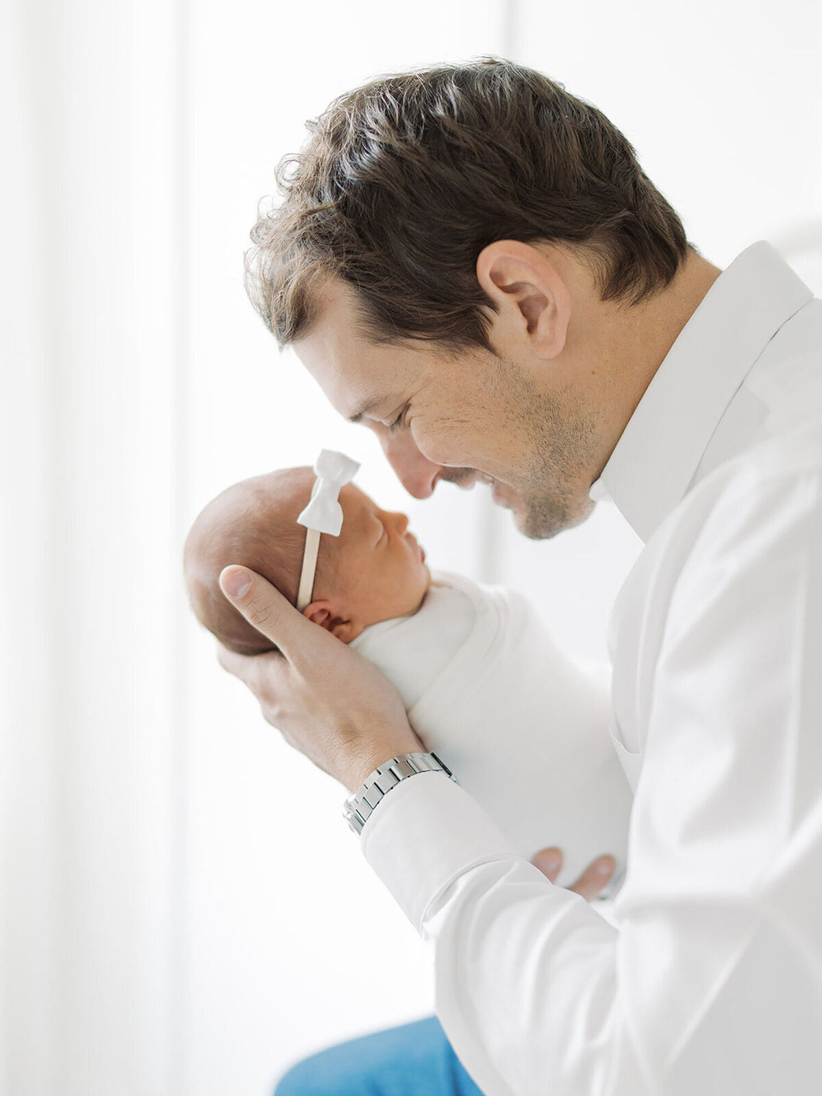 A father holding his newborn baby close to his face, gazing down at the baby with a loving expression