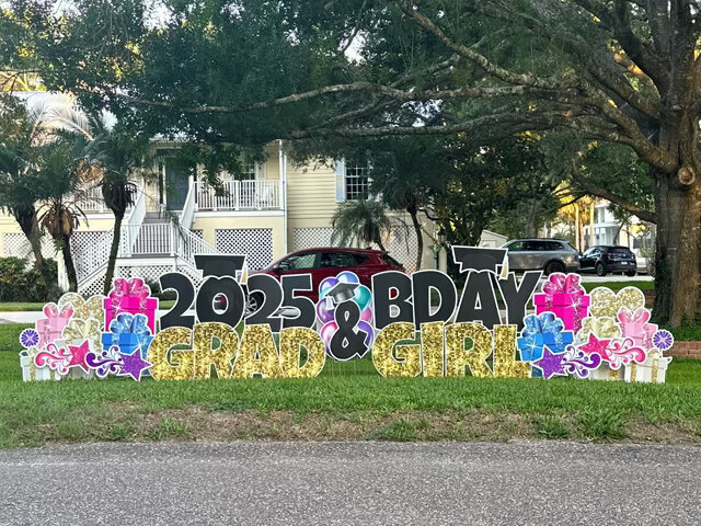 Combination birthday and graduation yard sign for girl with gold letters, colorful stars, and gift boxes in Windermere, Florida