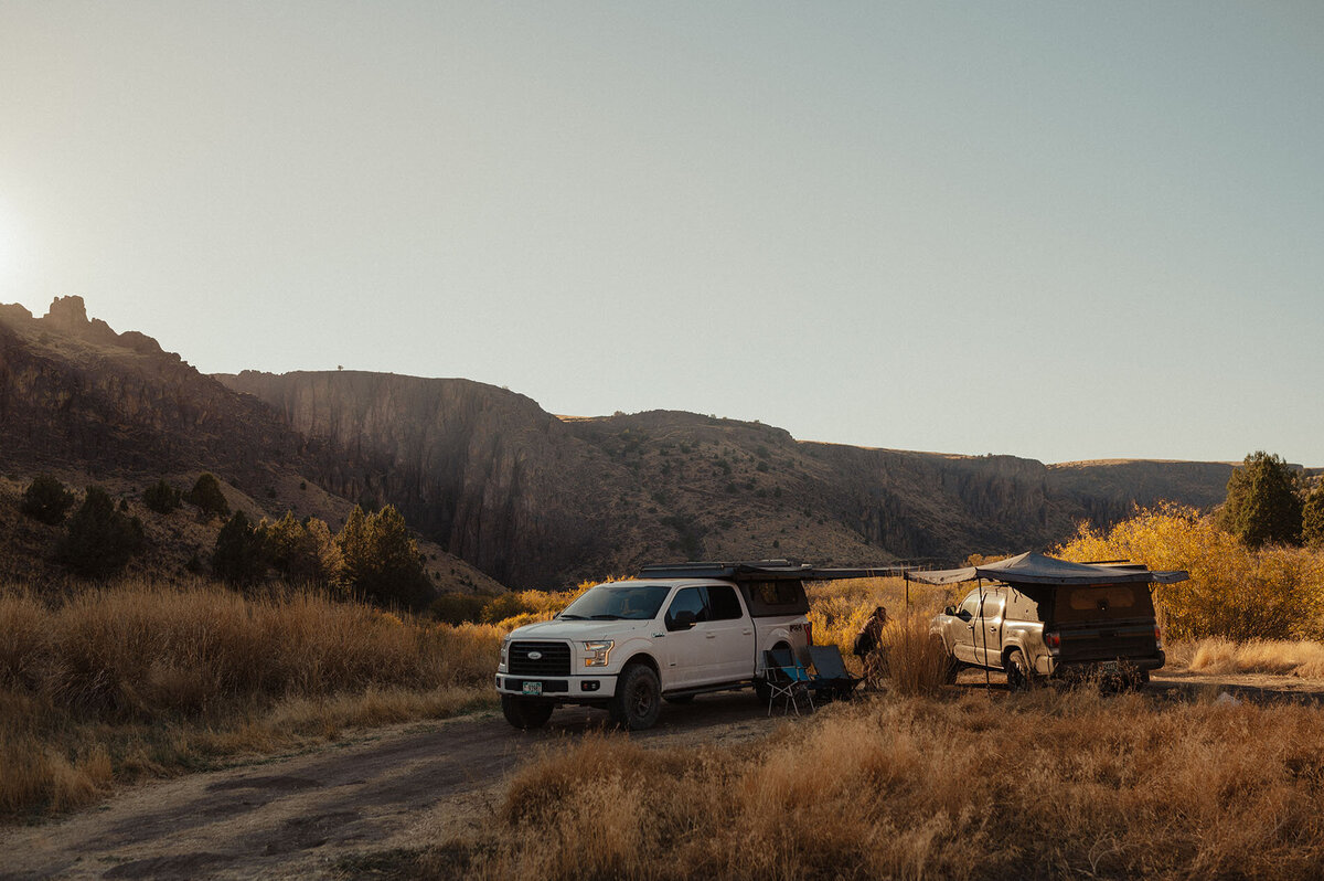 trucks with campers are parked in the golden sun with the towering cliffs behind them in Moab, Utah