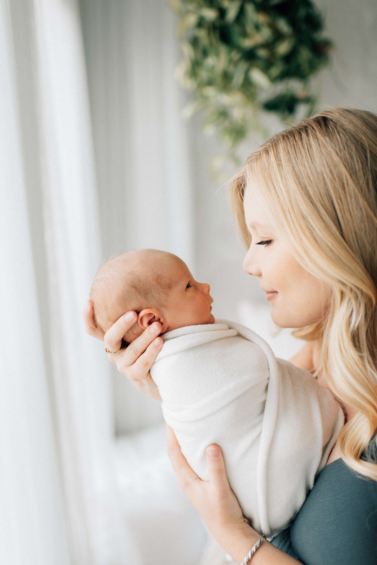 profile of mom standing by a window with baby swaddled in her hands