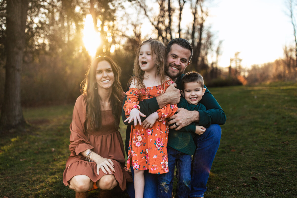 A girl in a bright orange dress embraces her dad during a family Portrait session held outdoors in a park near Pittsburgh Pennsylvania
