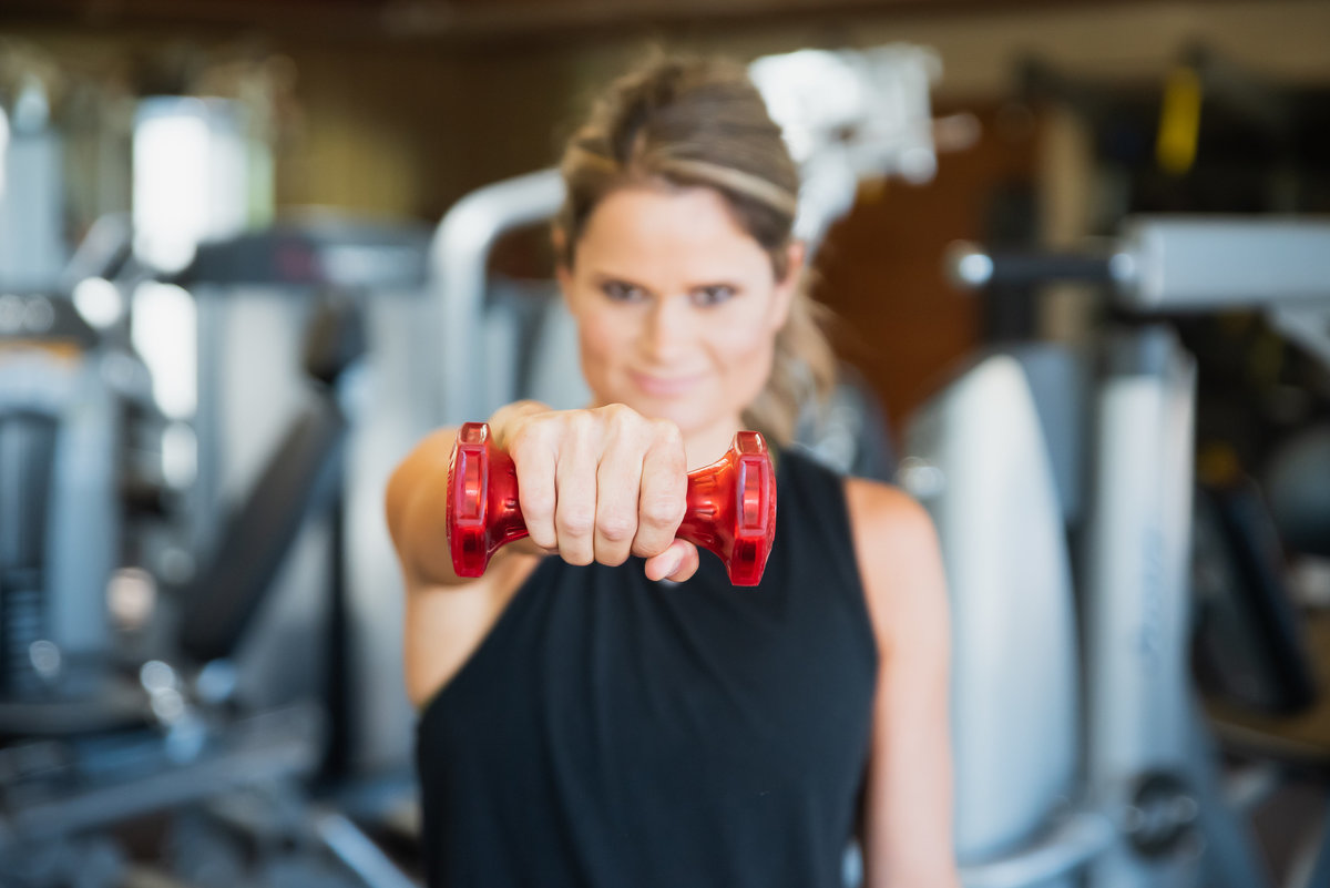 stylized lifestyle headshot image of health coach holding red weight out toward camera