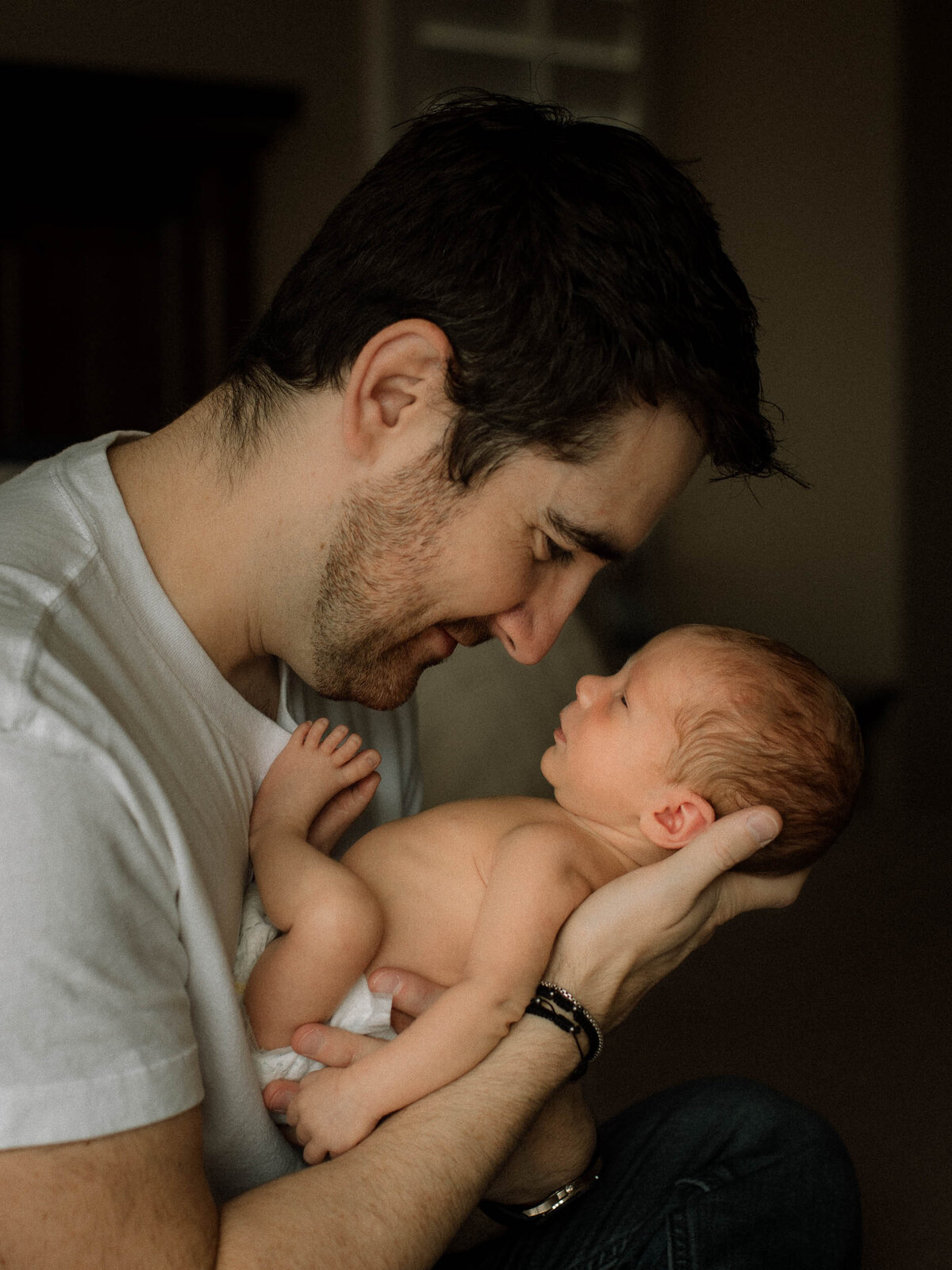 Dad gazing into baby's eyes while holding him face to face in hands.