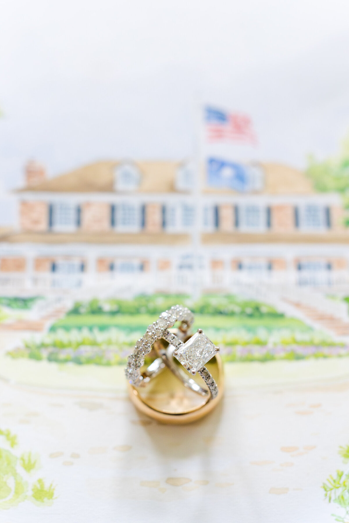 wedding rings resting on top of a painting of a wedding venue