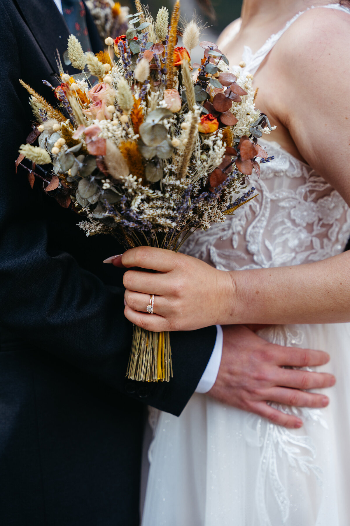 Bride holding dried flower bouquet in lace wedding dress