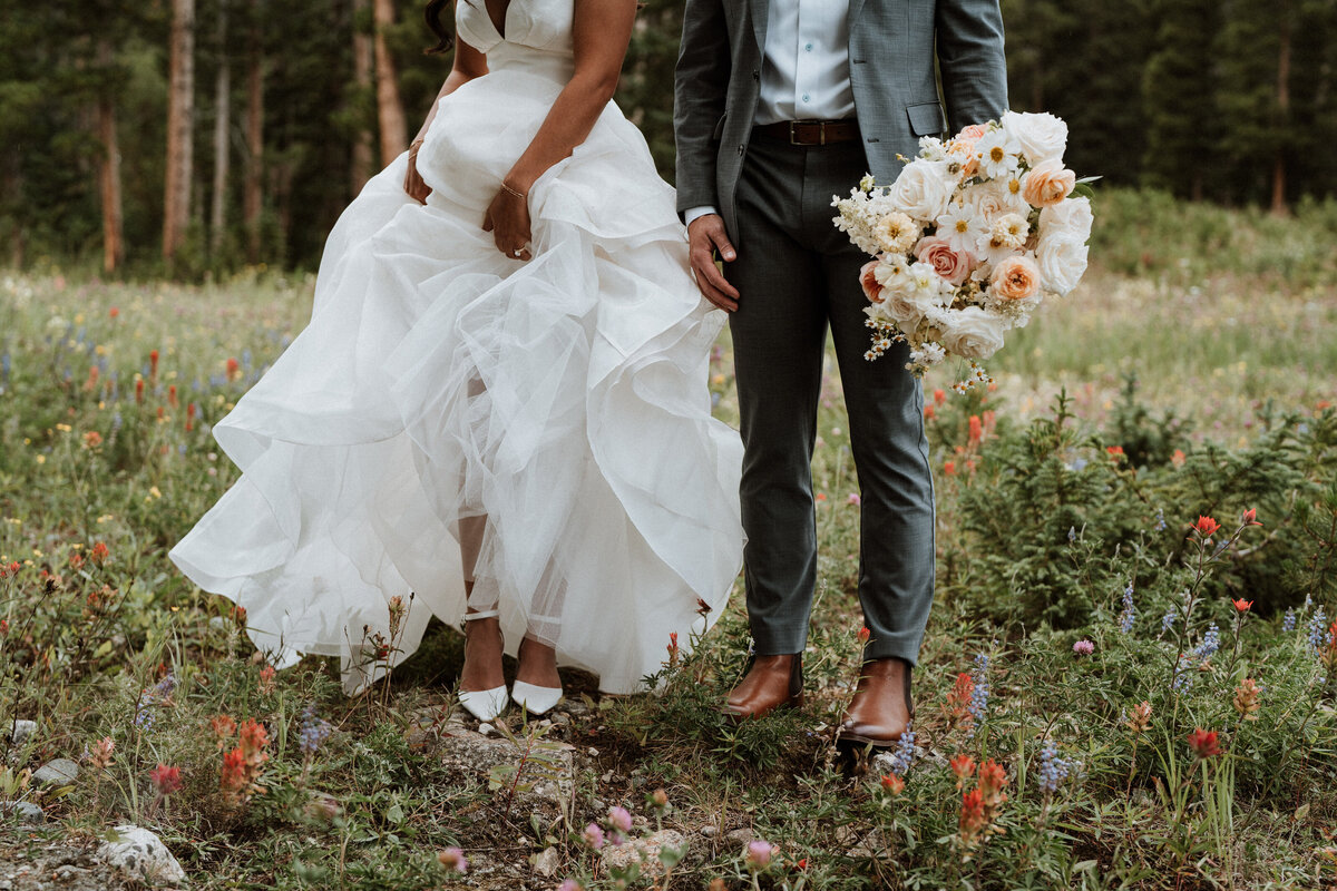 Close-up of bride and groom in wildflowers with lush forest backdrop in Breckenridge, Colorado. 