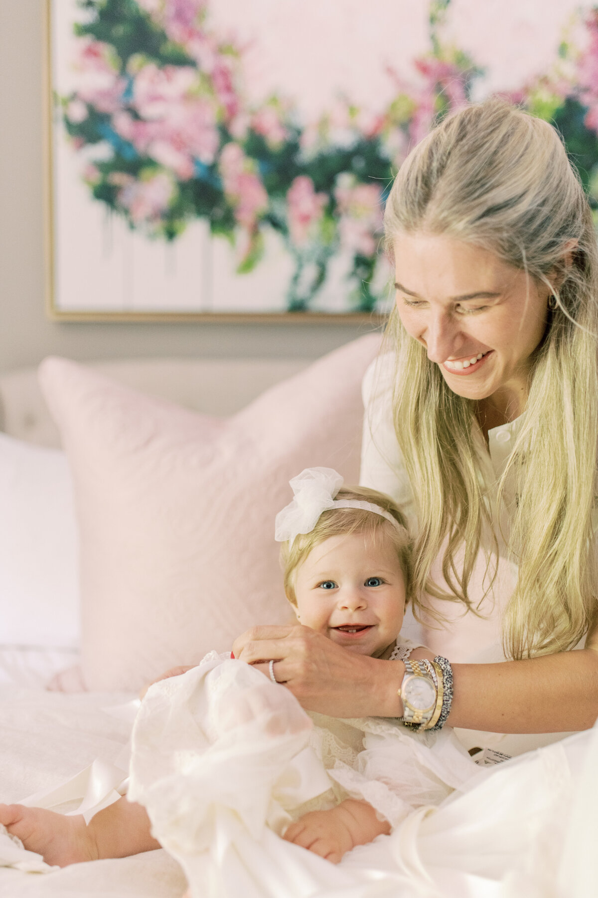 Mother and daughter share a luminous moment on baptism morning, bathed in soft Oakville light beneath a floral painting.