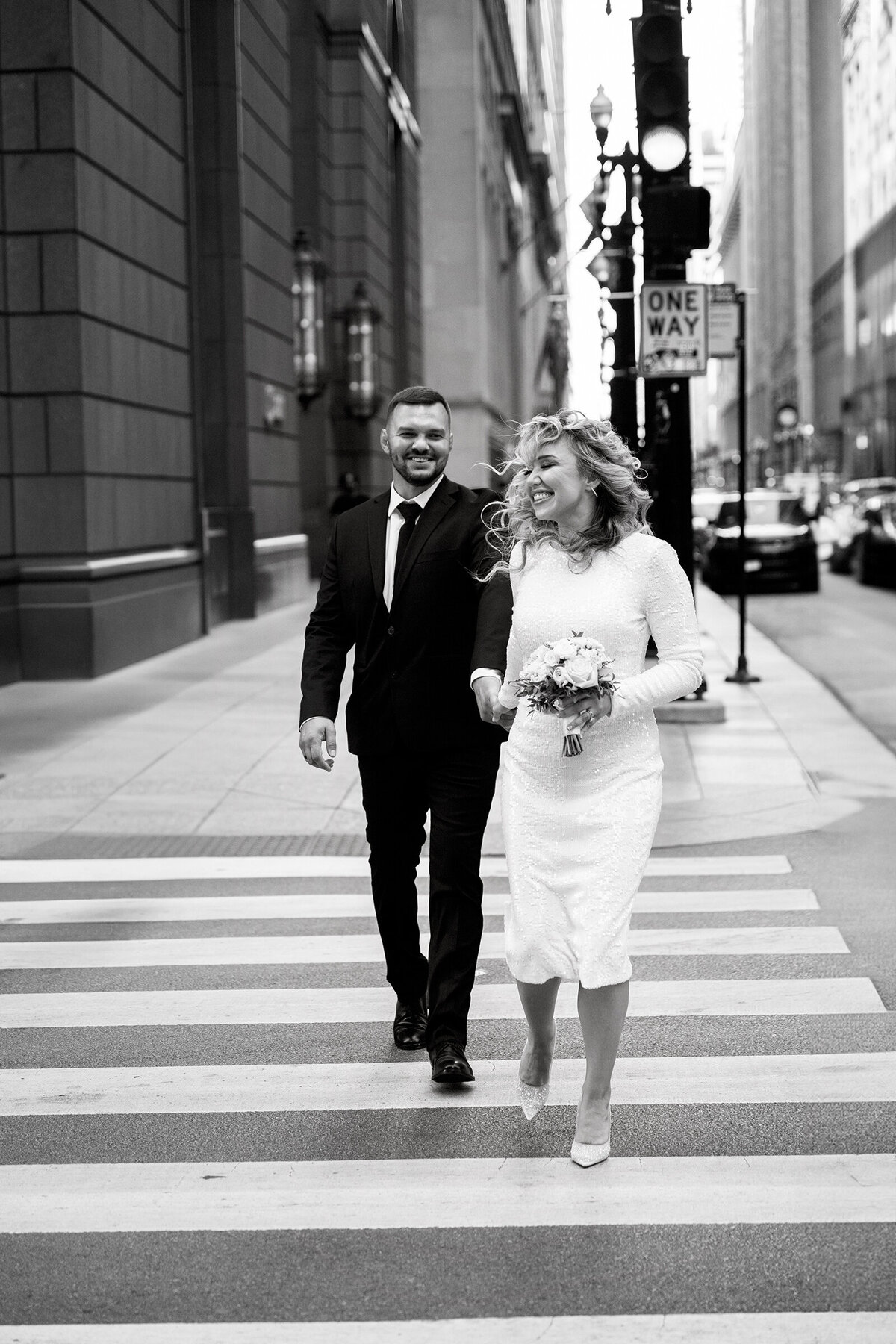 Candid black and white picture of groom and bride crossing busy street of Chicago after elopement