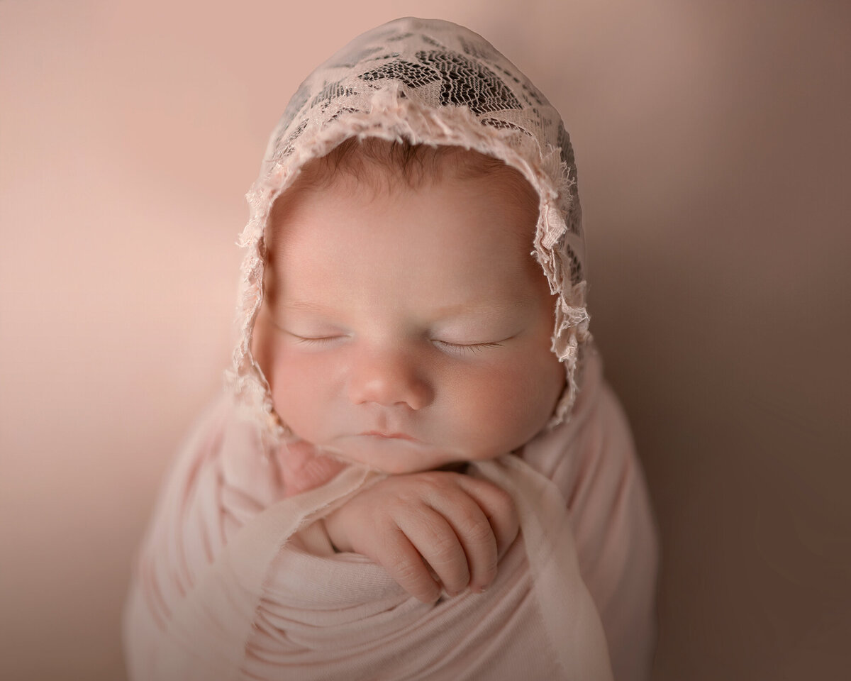 A newborn sleeping in a lace bonnet in matching swaddle