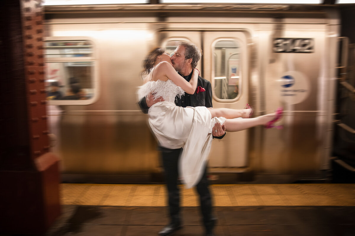 A bride and groom pose in front of a moving subway train in New York before their wedding