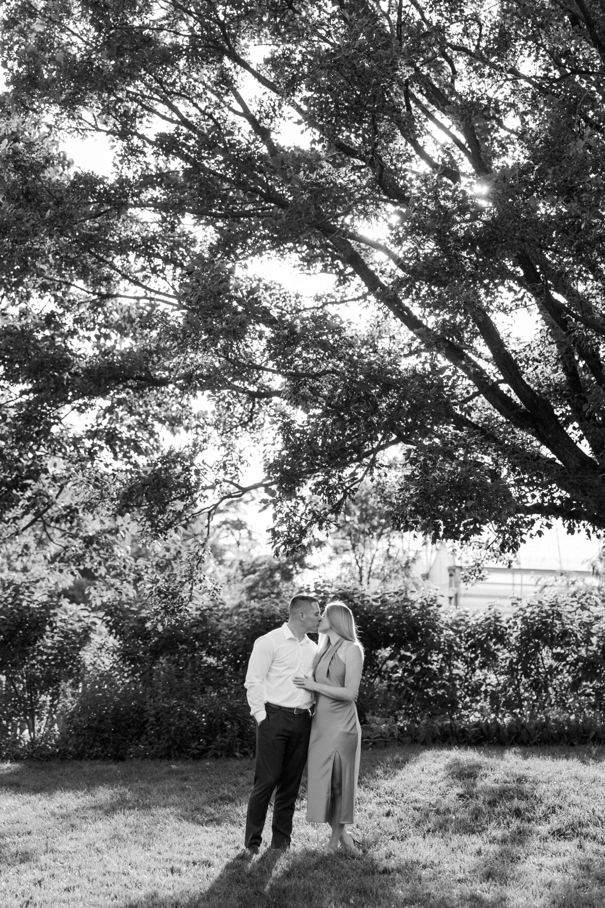 Black and white image of engaged couple kissing surrounded by lush Columbus garden shot by Philadelphia photographer.