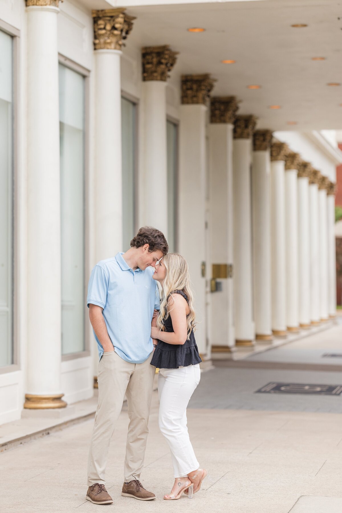 A happy engaged couple snuggles under an overhang with ornate columns