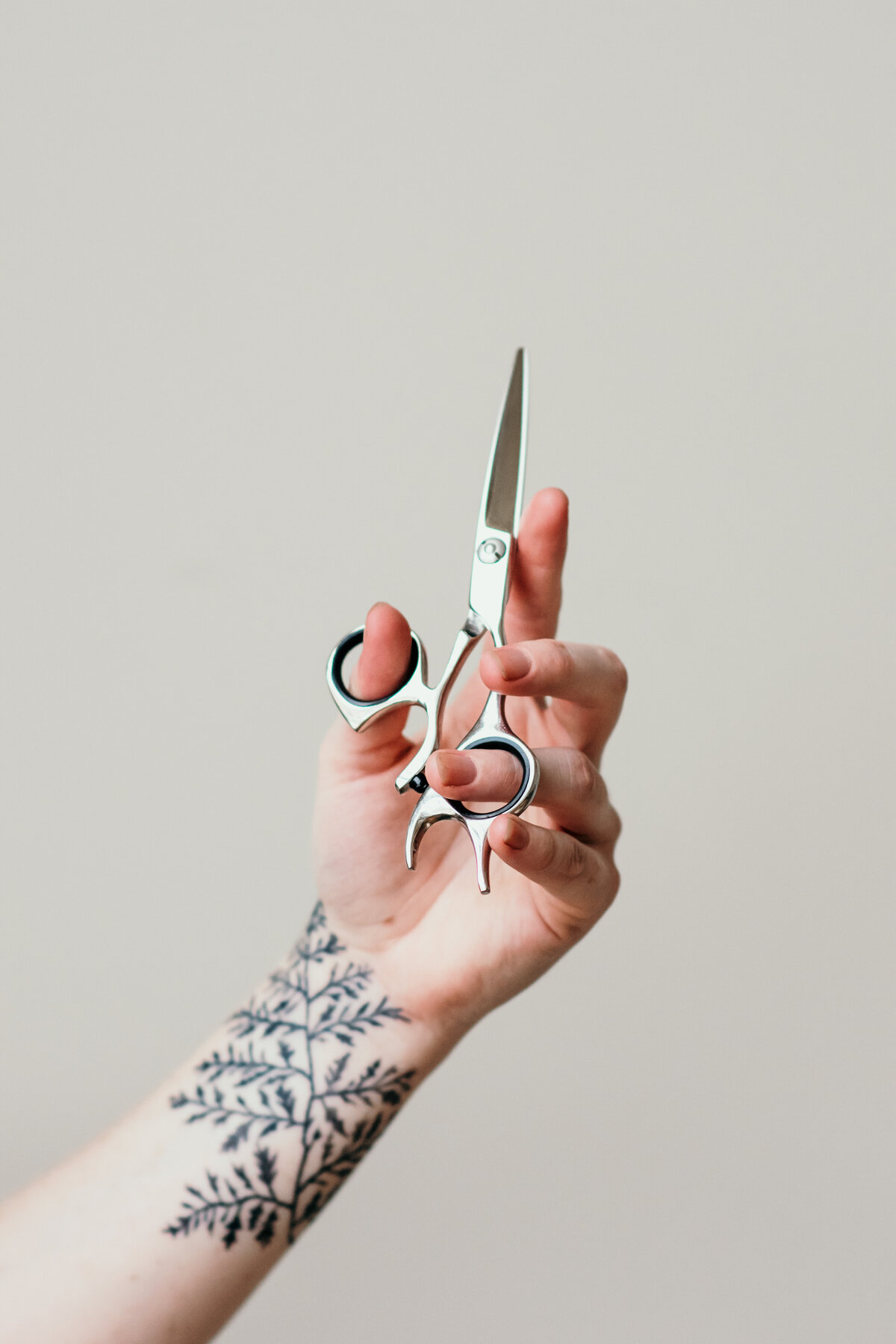 hairstylist with fern tattoo holding scissors