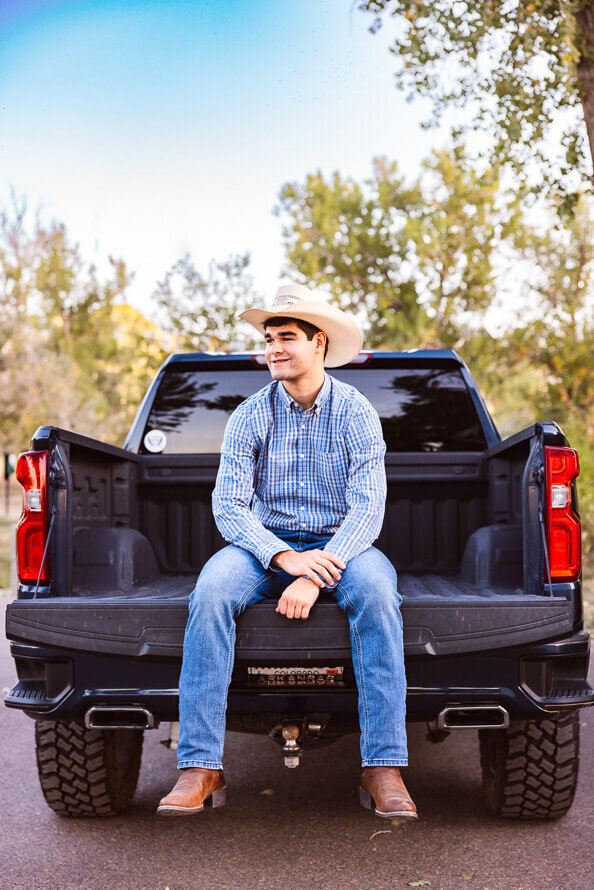 Senior boy with a cowboy hat sits in the bed of his truck.