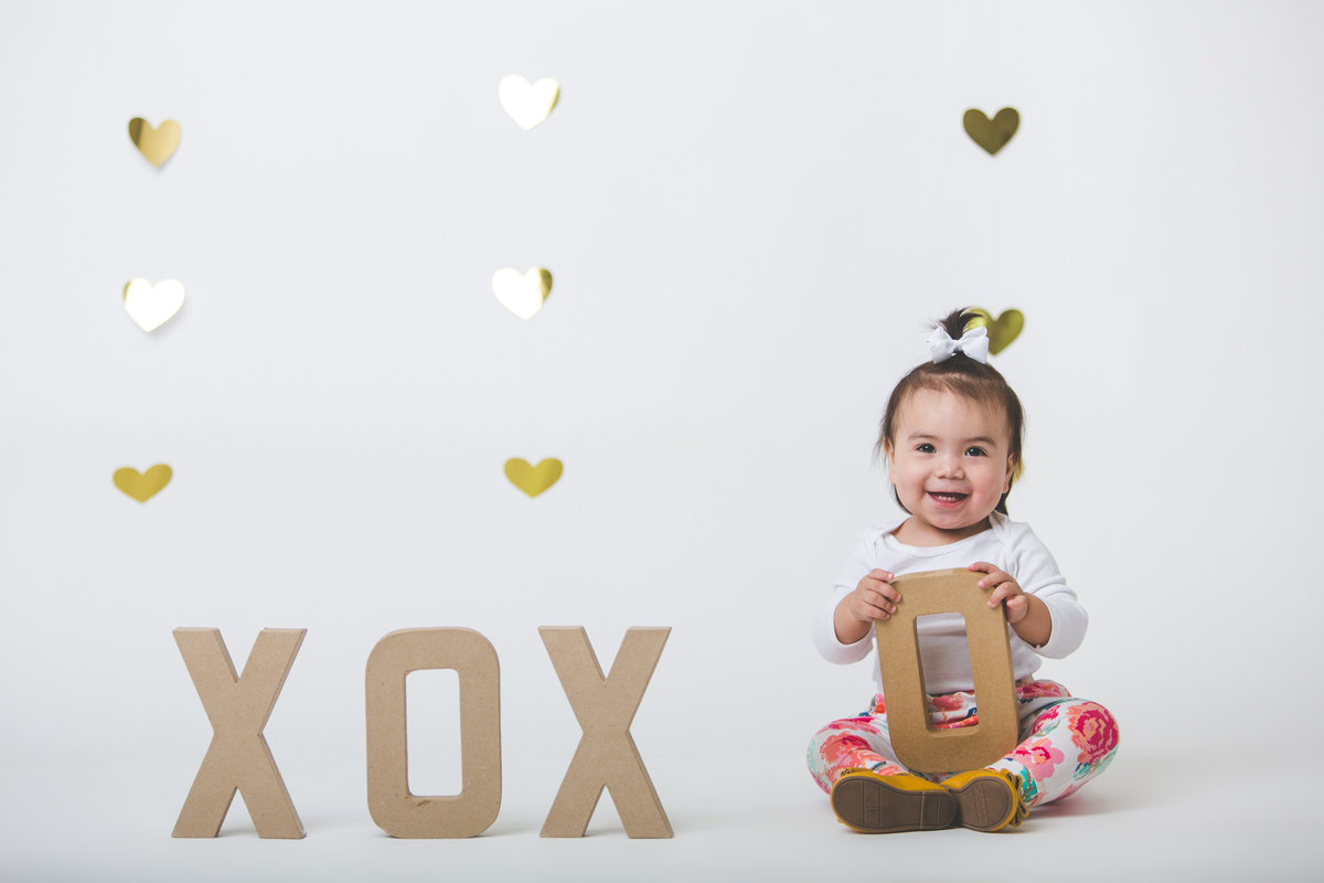 Baby with XOXO letter props in front of a heart backdrop in photography studio