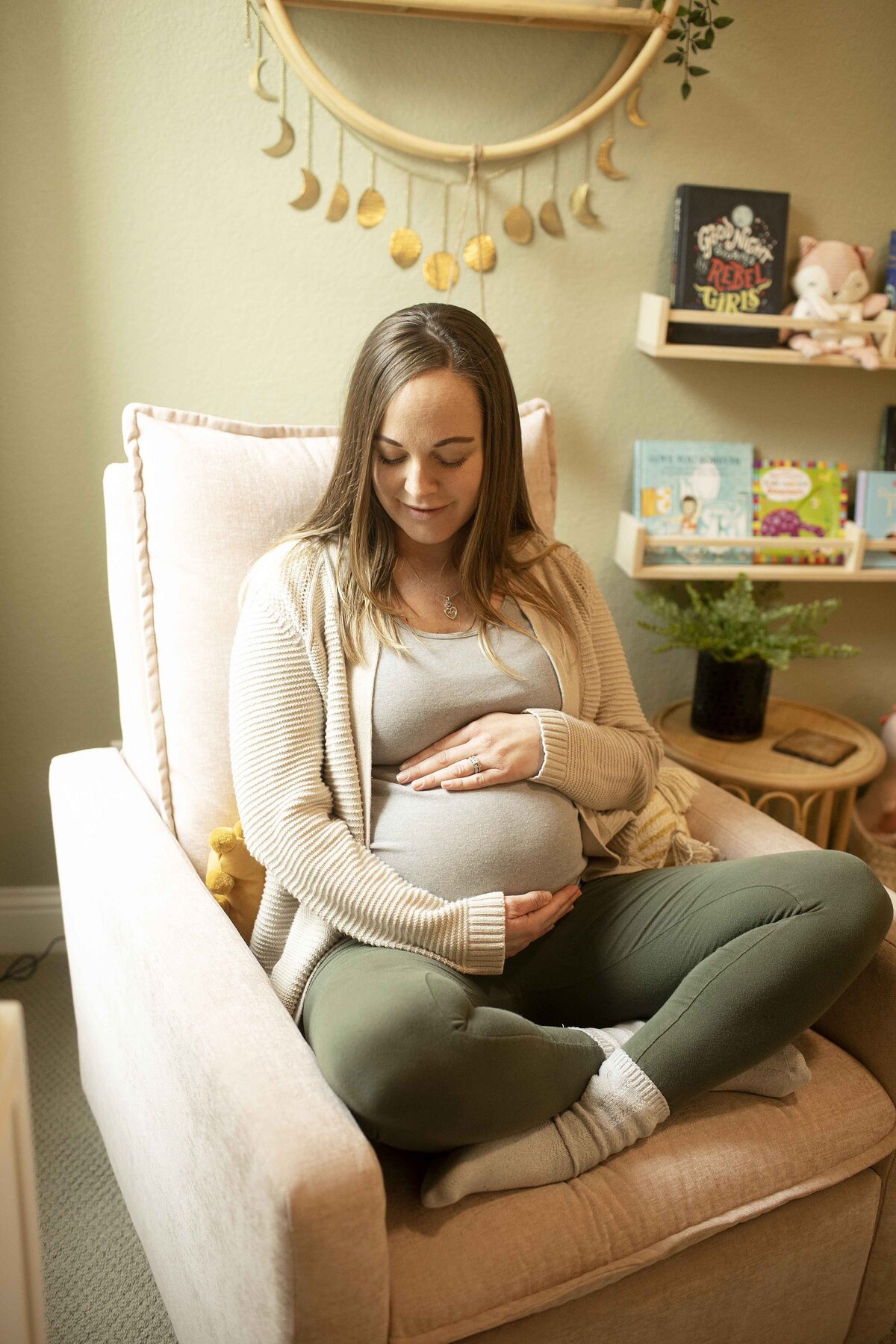 A tender maternity moment of mom in the nursery, lovingly touching her belly while gazing around at the beautifully prepared space for her little one, captured by Chunky Monkey Photography.