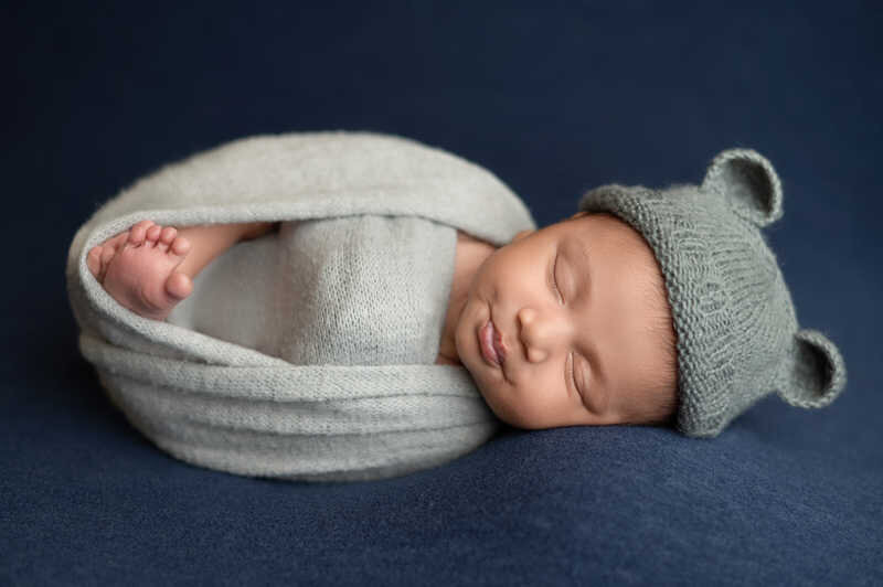 Newborn baby swaddled in blue wrap resting on neutral blanket during Houston newborn photoshoot