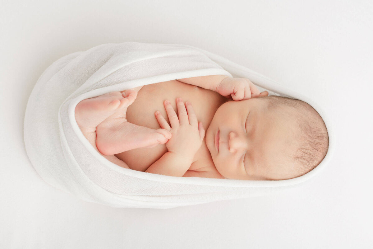 Baby wrapped up in a little cocoon with hands and feet showing on a white blanket at his Portland Oregon newborn photos