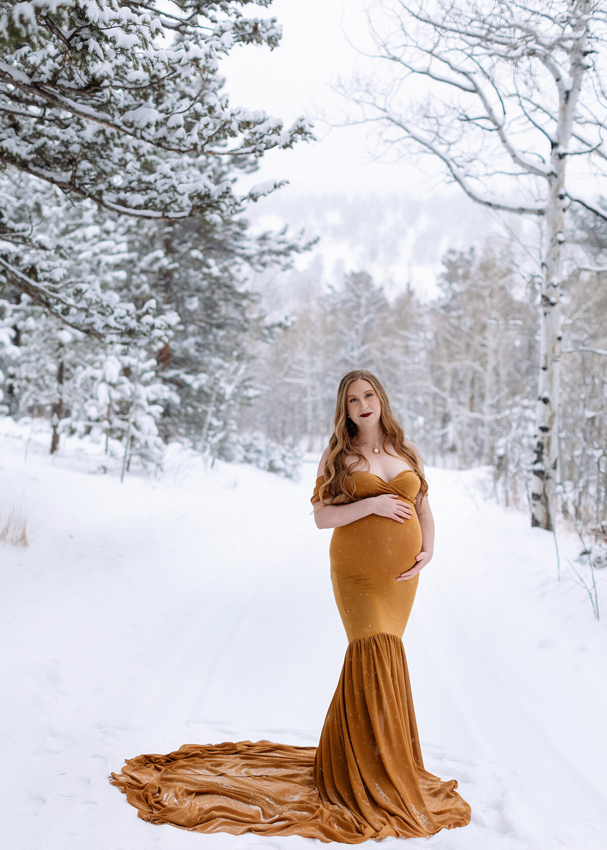 pregnant mom in maternity dress standing in a snowy mountain meadow in estes park posing for her maternity photographer