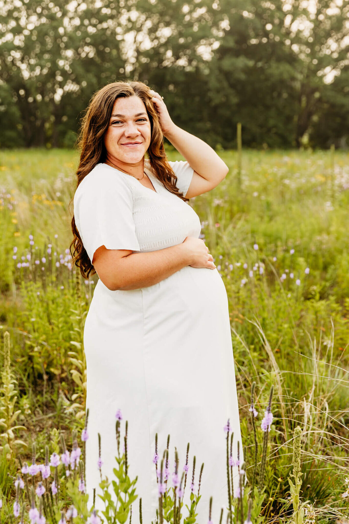 expecting mom in a white dress resting hand on her baby bump in a wildflower field near Green Bay